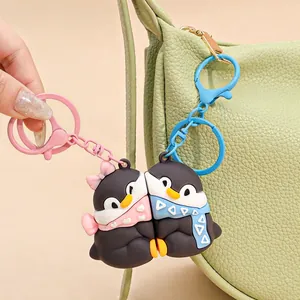 Cute magnetic penguin couple keychains in pink and blue hanging on a green textured bag