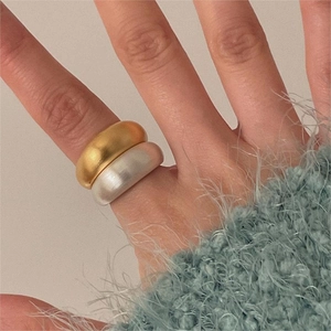 Detail of chunky gold and silver brushed rings worn with a blue knit sweater
