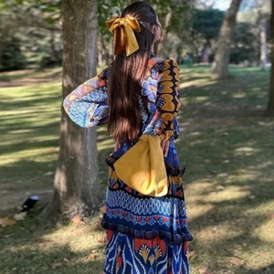 Detail of bohemian print long sleeve dress with yellow bow hair accessory in a park
