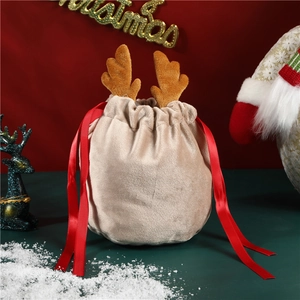 Beige velvet Christmas reindeer gift bag with red satin drawstring on snowy backdrop