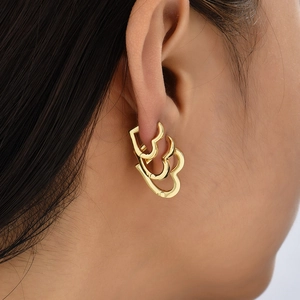 Macro view of triple layered hollow heart gold earrings worn on a female ear