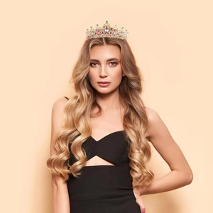 Close-up of a rainbow rhinestone crown worn by a model against a beige background