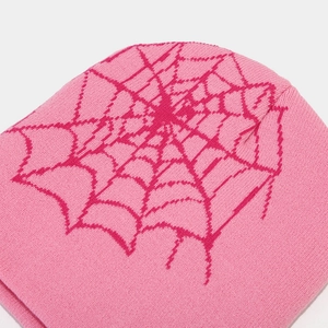 Detail of pink knitted beanie featuring a dark purple spider web pattern and soft texture