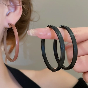 Detailed close-up of large geometric round hoop earrings in brown and black leather finish