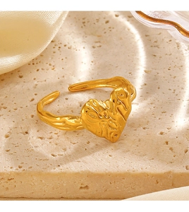 Close-up of golden heart ring with irregular texture on light satin and stone