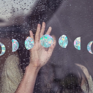 Detailed holographic moon phase window film reflecting rainbow colors on rainy glass surface