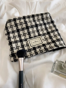 Close-up of black and white tweed cosmetic bag with Pleasant Time logo and zipper