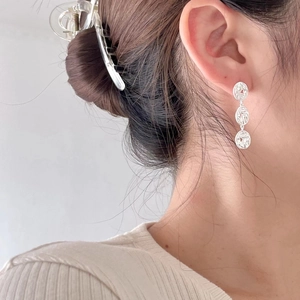 Close-up of three-tier textured silver circular drop earrings worn by a female model