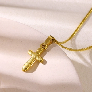 Detailed close-up of a golden cross necklace on a textured pink stone base
