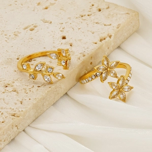 Detailed close-up of gold leaf and flower rings with sparkling zircons on travertine stone