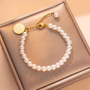 Elegant 18K gold-plated pearl bracelet with a round lucky charm on a jewelry box