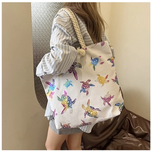 Detail of white canvas tote bag featuring a colorful turtle print and thick rope handles