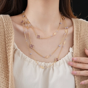 Detail of layered gold necklace with purple beads and clover-shaped square pendants
