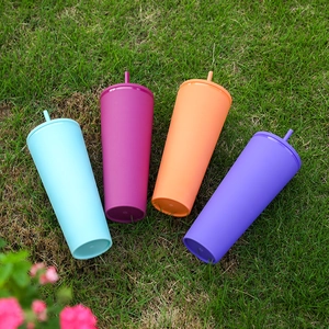 Colorful matte double-layer plastic tumblers with straws set on a fresh green lawn