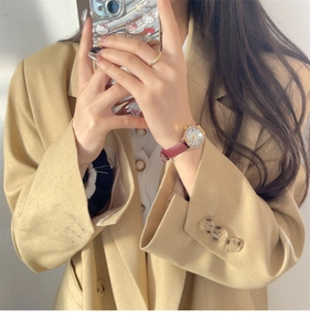 Elegant gold watch with red leather strap and diamond bezel worn with beige blazer