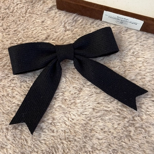 Detail of a black knitted bow hair clip with ribbed texture on a soft white background