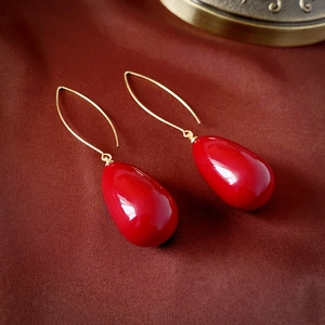 Macro shot of elegant red teardrop earrings with gold hooks on silk fabric