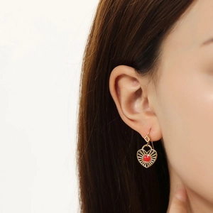 Gros plan de boucles d'oreilles cœur dorées avec pierres rouges portées par un mannequin
