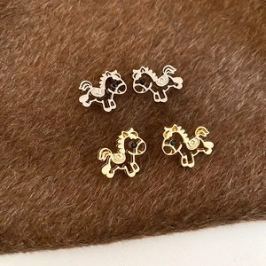 Detailed view of hollow horse-shaped studs in gold and silver finish on a textured background