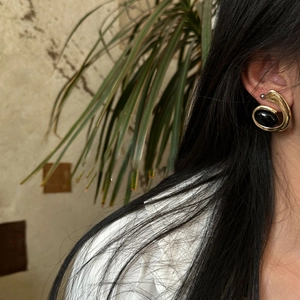 Close-up of golden spiral earrings with black oval resin stone worn on model ear