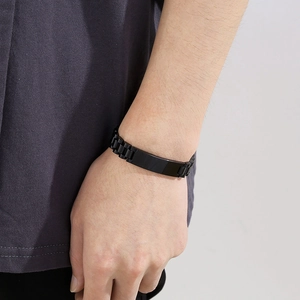 Close-up of a black stainless steel link bracelet with a smooth metal plate on a male wrist