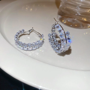 Détail de créoles argentées avec double rangée de zircons sur une assiette blanche