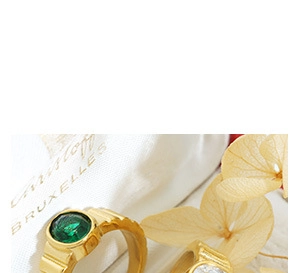 Macro shot of gold-plated rings with green emerald stone and textured geometric band