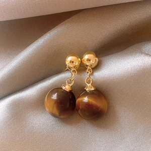 Detail view of 18k gold plated earrings with tiger eye stones on champagne silk