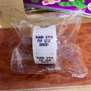 Close-up of thank you stickers in a roll with black font and red hearts for packaging