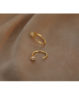 Macro shot of gold-plated earrings with clear cubic zirconia on beige fabric texture