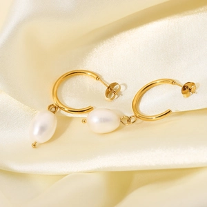 Macro detail of gold C-shape earrings with white oval pearl pendants on beige silk fabric