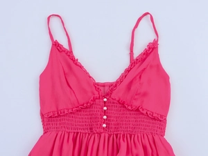 Détail de robe rose avec boutons nacrés, décolleté en V à volants et taille smockée