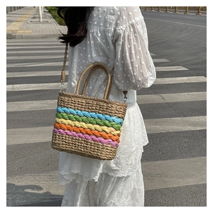 Street style shot of a rainbow striped straw handbag with shoulder strap and handles
