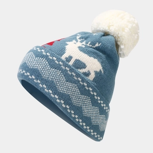 Macro detail of winter knit hat with white reindeer jacquard and plush pom-pom