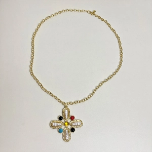 Detailed view of a gold cross pendant with colorful gemstones and pearls on a white surface