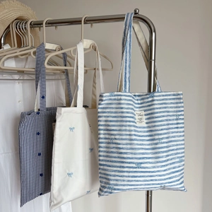 Detail view of cotton tote bags featuring blue stripes and bow embroidery designs