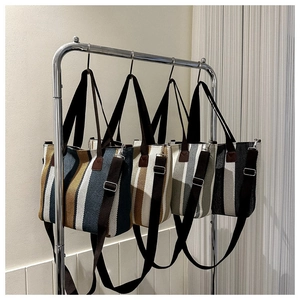 Detailed view of four striped canvas tote bags with adjustable straps on a metal rack