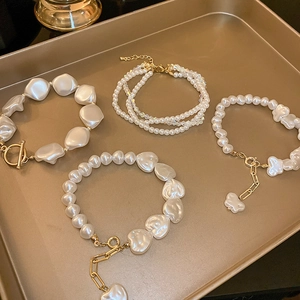 Detailed macro view of pearl bracelets with OT buckle and heart charms on a golden tray