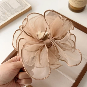 Détail d'une pince à cheveux à nœud en tulle champagne multicouche tenue à la main