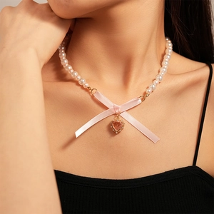 Close-up of the elegant pearl necklace with a pink bow and heart pendant on model