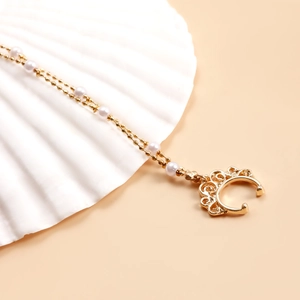 Détail d'une chaîne de nez dorée à double couche avec perles posée sur un coquillage