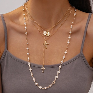 Detail of layered gold-tone necklace with faux pearls, Virgin Mary icons and cross charm