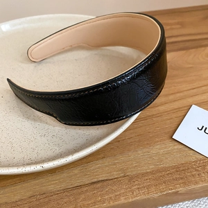 Detail of black pleated leather headband featuring contrast orange stitching and soft texture