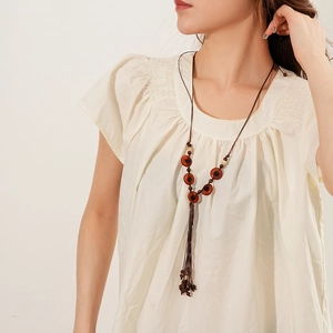 Detail of bohemian long necklace featuring wood beads and a tassel pendant on a model