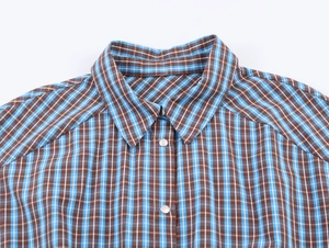 Dettaglio del colletto di camicia a quadri blu e marroni con occhielli in metallo