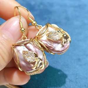Detailed close-up of pink baroque pearl earrings with golden zircon-studded leaf accents