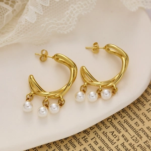 Gold C-shaped titanium steel earrings with triple pearl pendants on a ceramic tray