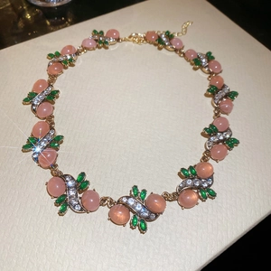 Close-up of pink oval resin and green leaf gemstones on a gold necklace chain