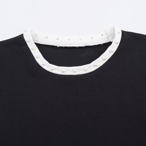 Dettaglio di un girocollo su una t-shirt nera con eleganti accenti di perle bianche