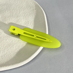 Neon green metal hair clip in spade shape on a white ceramic plate with a gray background